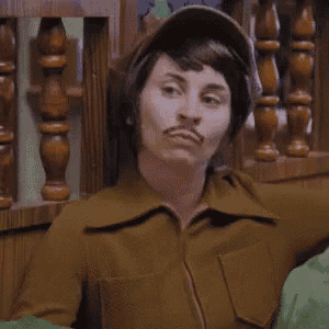 a woman with a mustache is wearing a brown jacket and a hat .