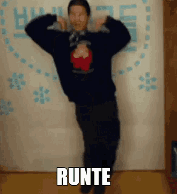 a man in a black sweater is dancing in front of a wall with the word runte on it .