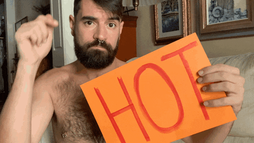 a shirtless bearded man holds up a sign that says hot