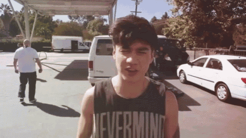 a man wearing a tank top that says nevermind stands in a parking lot