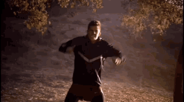 a man wearing a black nike jacket is standing in the woods