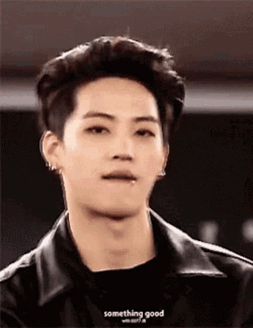 a young man wearing a leather jacket and a black shirt is making a face .