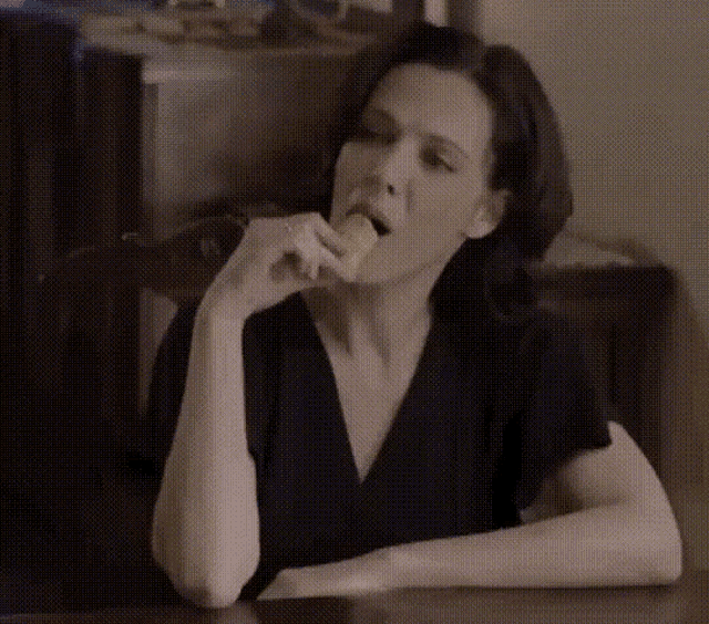 a woman in a black shirt is sitting at a table eating a snack
