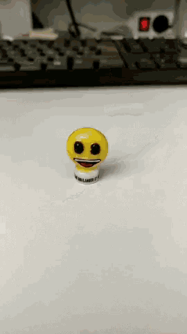 a yellow smiley face on a white surface with a keyboard behind