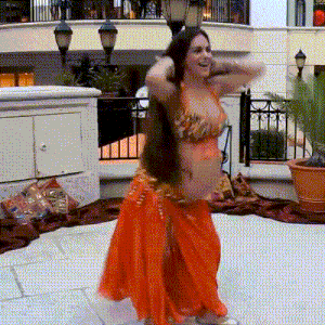 a belly dancer in an orange outfit is dancing on a sidewalk