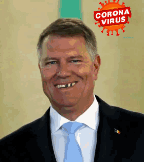 a man in a suit and tie smiles in front of a corona virus logo