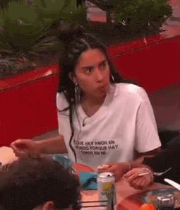 a woman in a white t-shirt is sitting at a table with a can of beer .