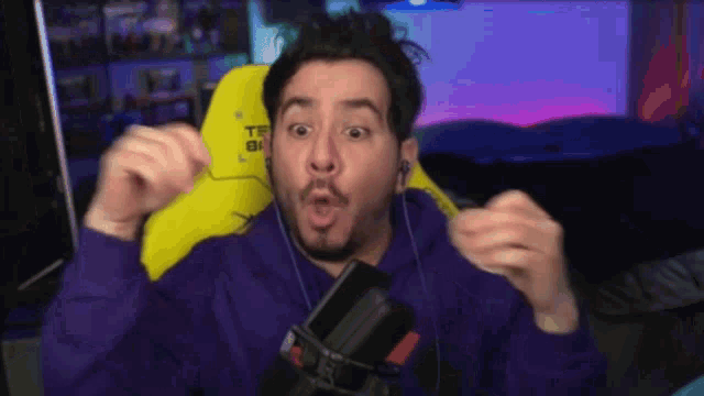 a man in a purple hoodie is sitting in a yellow chair with a tf logo on it