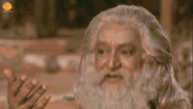 a man with gray hair and a beard has a tlak logo on the bottom left