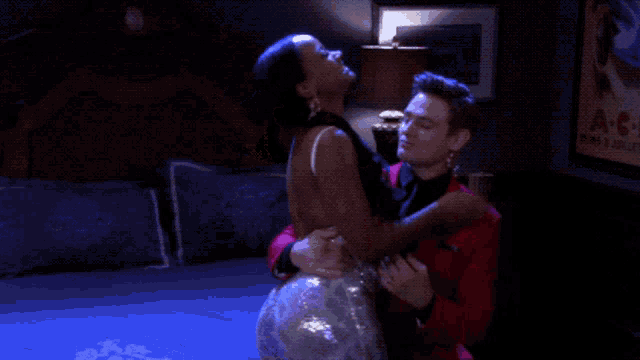 a man in a red suit holds a woman in a silver dress