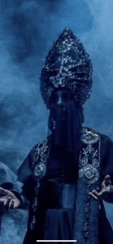 a man with a beard and a crown on his head stands in the dark
