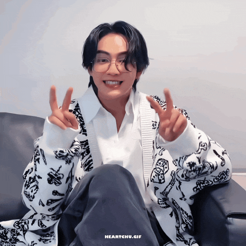 a young man wearing glasses and a white shirt is sitting in a chair and giving the peace sign