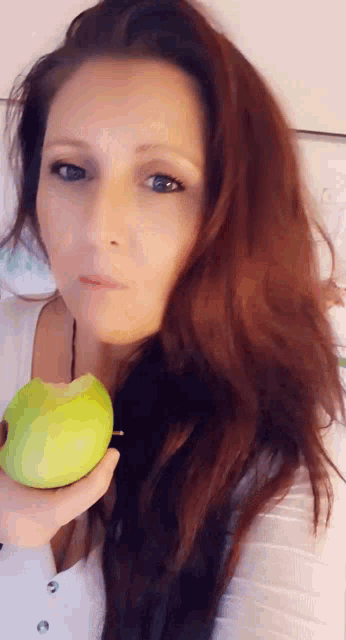 a woman with long red hair is holding a green apple in her hand