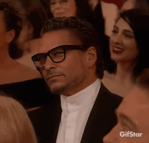 a man wearing glasses and a tuxedo is sitting in a crowd of people with a gif star watermark