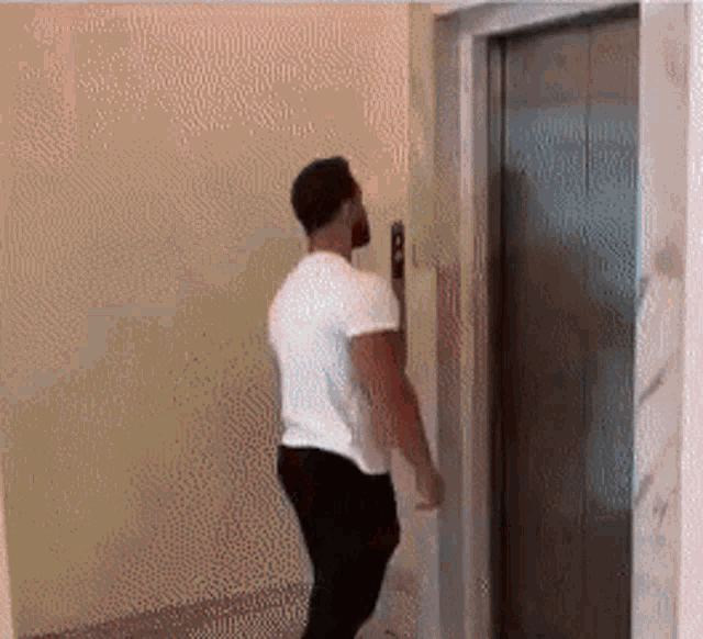 a man in a white shirt is standing next to an elevator .