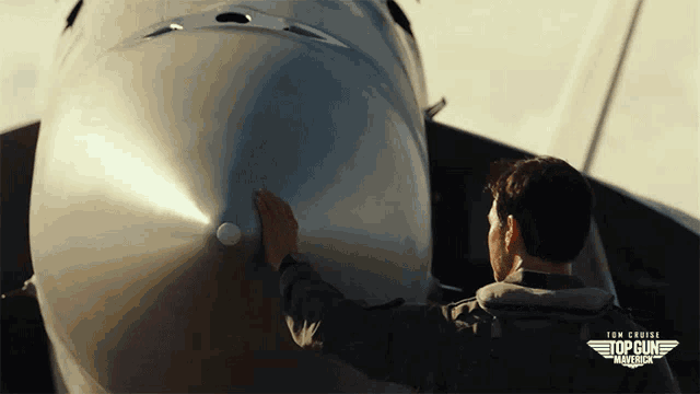 a man is touching the nose of a plane that says top gun maverick on it