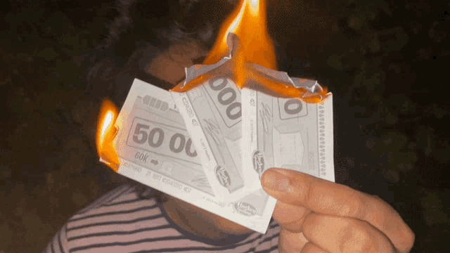a person is holding a burning 50 and 60k bill