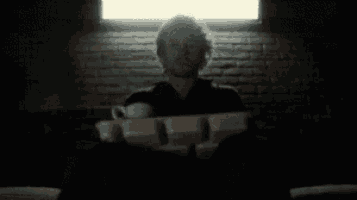 a man is sitting in a dark room holding a cup and a tray of food .