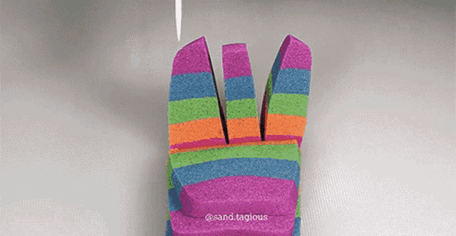 a rainbow colored block of sand is being cut into pieces .