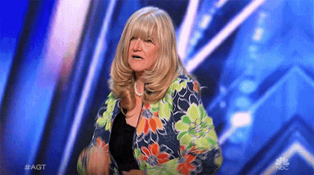 a woman is standing on a stage wearing a colorful jacket and a black shirt .