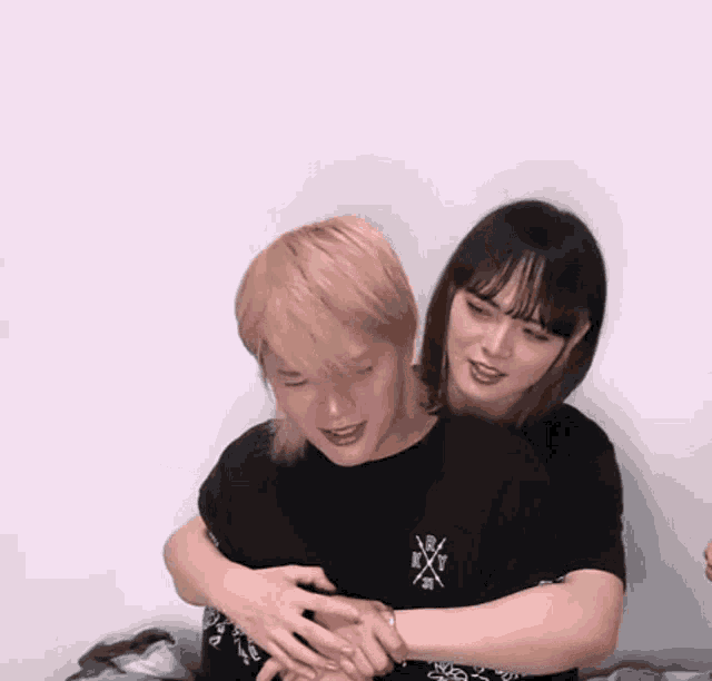 a woman is hugging a man who is wearing a black t-shirt that says x on it