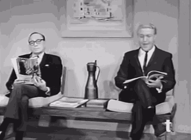 a man in a suit sits on a bench reading a book