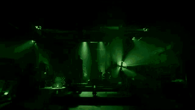 a man is standing on a stage in a dark room with green lights shining on him .