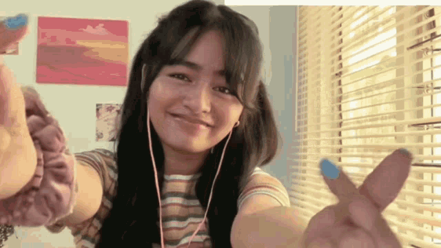 a woman wearing headphones and blue nail polish is making a peace sign
