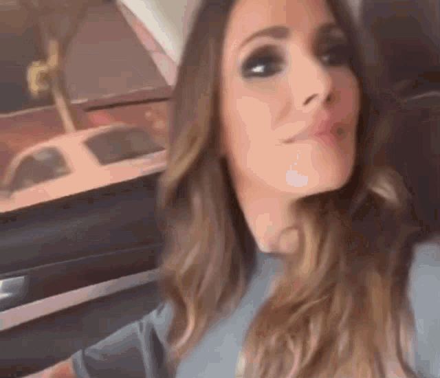 a woman with long hair is sitting in the back seat of a car looking at the camera .