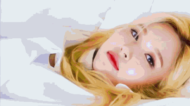 a woman with blonde hair and red lipstick is laying on a bed looking at the camera .