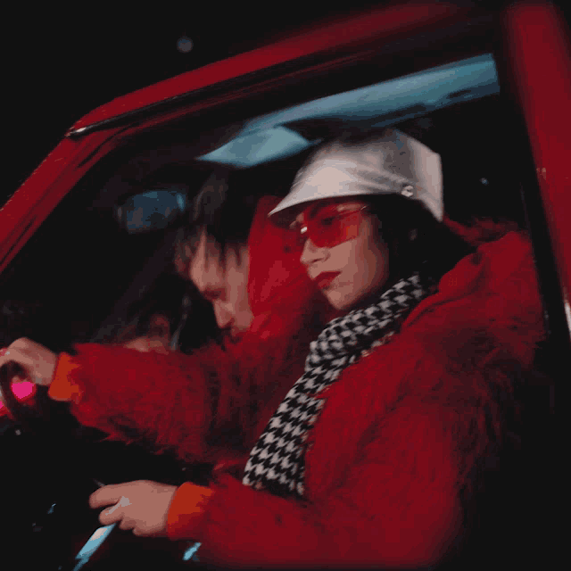a woman wearing red sunglasses and a white hat is driving a car