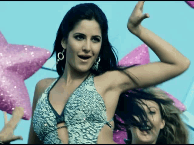 a woman in a bikini top is dancing in front of a blue sky