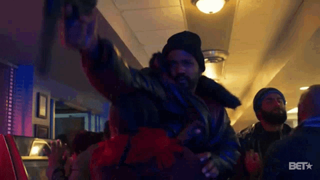 a man in a leather jacket is standing in a crowd of people with the word bet on the bottom