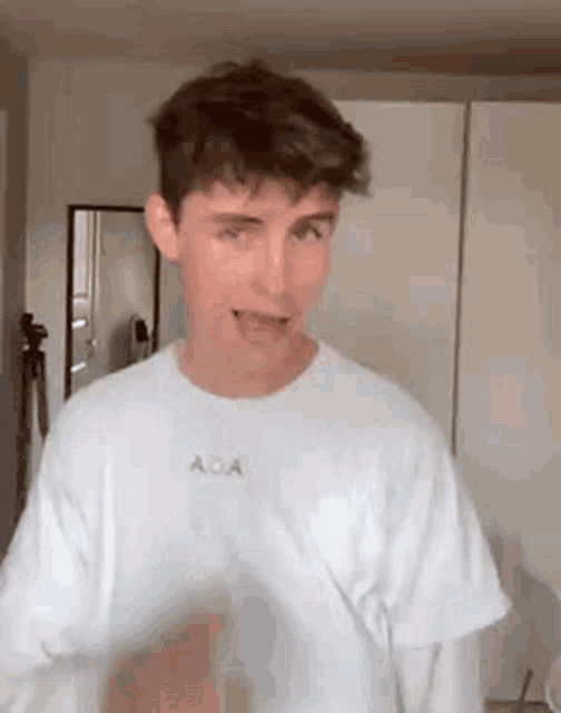 a young man wearing a white t-shirt is standing in front of a mirror and making a funny face .