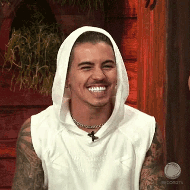 a man wearing a white sleeveless shirt with a hood is smiling for the camera