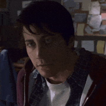 a man wearing a plaid shirt and a maroon hoodie looks at the camera