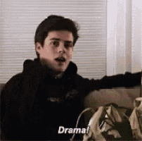 a young man is sitting on a couch talking to someone and saying `` drama '' .
