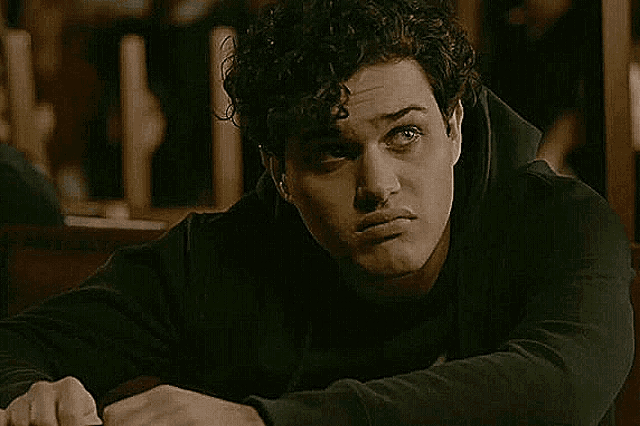 a young man with curly hair is sitting at a table with his head resting on his elbow .