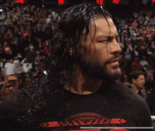 a man with long hair and a beard is smiling in front of a crowd in a stadium .