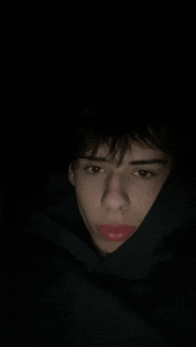 a young man with red lipstick on his lips is wearing a black hoodie and covering his face .