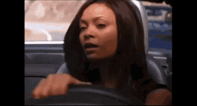a woman is sitting in the driver 's seat of a car and making a funny face .