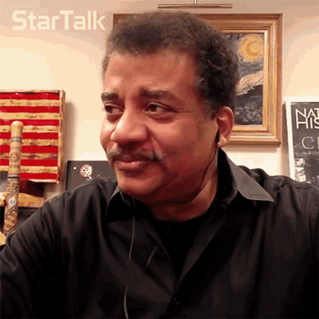 a man wearing a black shirt and ear buds looks at the camera with a startalk logo behind him