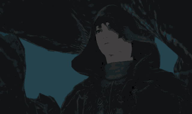 a man in a black hooded cape stands in a dark cave