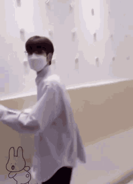 a man wearing a mask and a white shirt is standing in front of a white wall .