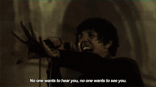 a man singing into a microphone with the words no one wants to hear you no one wants to see you below him