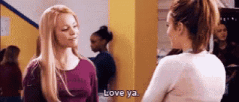 two women are standing next to each other in a hallway and talking .