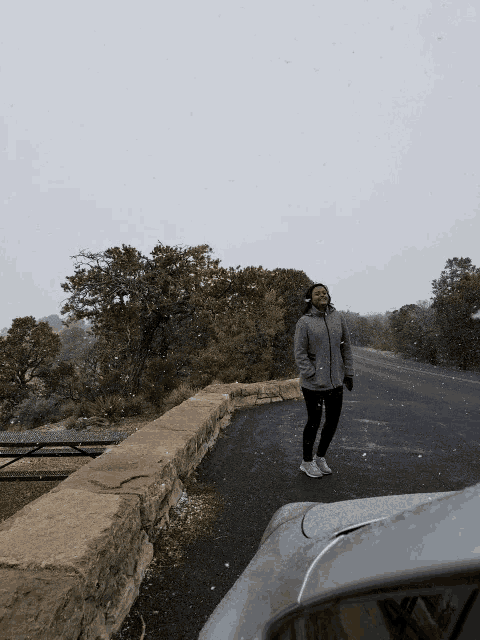a woman in a gray jacket is standing on a snowy road