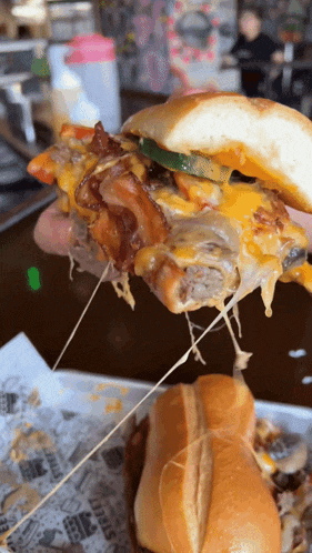 a close up of a person holding a sandwich with cheese pulled out of it