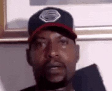 a man with a beard is wearing a baseball cap and looking at the camera .