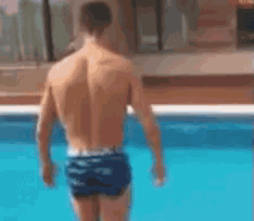 a shirtless man in blue swim trunks is walking into a pool